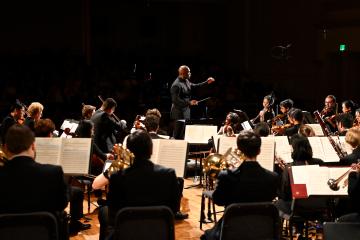 An individual conducts a group of classical musicians seated in an orchestra arrangement